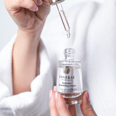 Hand druppelt Inveray Intensive Rebuilding Serum uit een glazen flesje voor intensieve hand- en nagelverzorging.